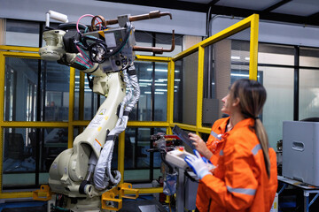 Girl engineer commissioning operating programming and looking at robot machine in the factory