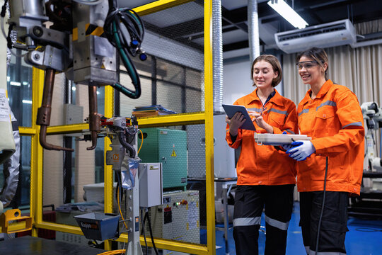 Girl engineer commissioning operating programming and looking at robot machine in the factory