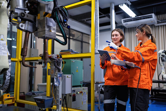 Girl engineer commissioning operating programming and looking at robot machine in the factory