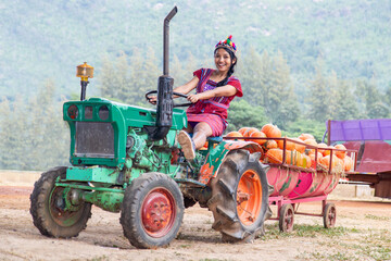 A cheerful woman in a traditional costume drives an old tractor with a load of harvest