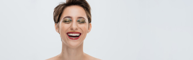 positive young woman with shiny makeup and short hair smiling isolated on grey, banner.