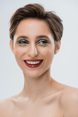 portrait of cheerful young woman with shiny makeup and short hair isolated on grey.