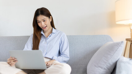 Woman using laptop to work or do homework at home with smiling face in her living room, Creating happiness at work with a smile, Live performance or video call with laptop, Work from home.