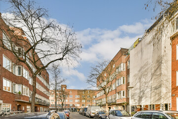 a city street with cars parked on the curbs and trees in the middle part of the street is bare