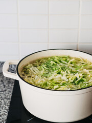 White ceramic frying pan with chopped cabbage in broth