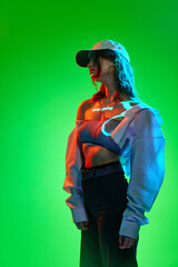 One sensual young girl wearing stylish clothes with digital neon filter lights with inscryption on body on bright green mode background. Vr reality