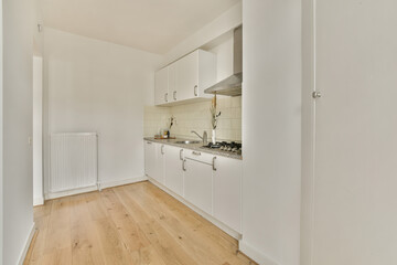 a kitchen area with white cabinets and wood flooring in an apartment or residential building, taken from the inside