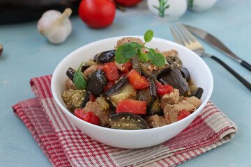 Meat stew with eggplant and tomatoes served in white bowl on blue background