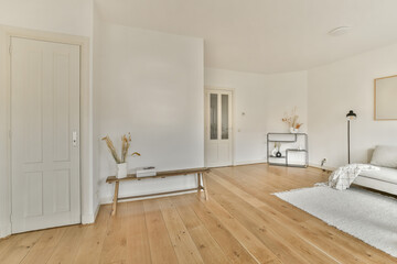 a living room with white walls and wood flooring in the center of the room, there is a bed on the right side