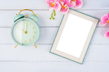 The Top view of blank photo frame and vintage alarm clock with pink color flower on wooden background, Save clipping path.