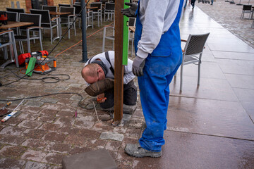 Metal worker spot welds on a steel beam outside on the ground in bad weather