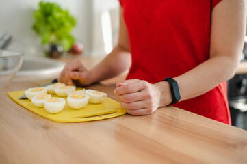 The girl cut boiled eggs in half on a yellow cutting board. Focus on the anterior eggs.