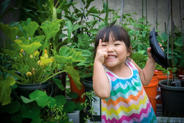 Young asian girl holding eggplant from home container vegetable garden