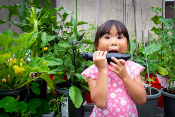 Young asian girl taking a big bite from eggplant from home container vegetable garden