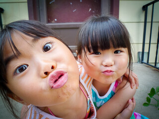 Two young asian girls hugging and making kissing gestures at the camera