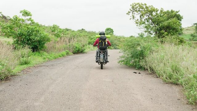 Back view traking shot of indian traveller with backpack riding motorbike near mountains - concept of relaxation, weekend holiday and freedom.