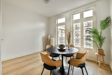 a dining table and chairs in a living room with large windows looking out onto the balcony area at an apartment