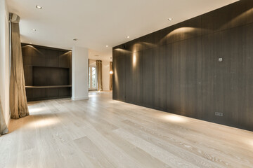 an empty living room with wood flooring and black cabinetd cupboards on the right side, there is light coming in through