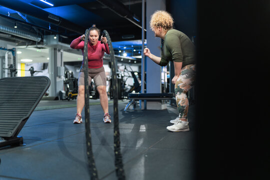 Two beautiful, overweight women push their limits during a workout, supporting each other every step of the way on their journey toward improved health and fitness. Using battle rope.