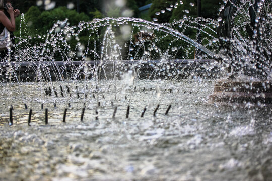 Splashing water in the fountain at summer city public urban park. Water jets abstract image close up. Thin jets of pure clear aqua splashes flying upwards under pressure. Gray stone wall background.