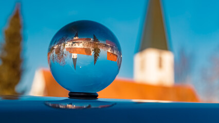 Crystal ball landscape shot with a church and reflections on a car roof at Mamming, Isar,...