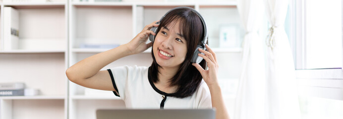 Young Asian woman happily listening to music through headphones, Girl was enjoying listening to her favorite music and rocking to the beat of the music, Stress relief, Happiness in life.