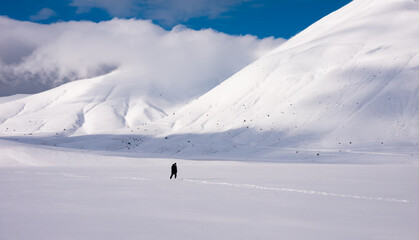 Fototapeta na wymiar Winter landscape, man walking in snow valley surrounded by hills