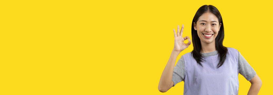 Young asian woman over yellow background doing ok sign with hands, OK symbol, Welcome, Agree, Join, Do as instructed, Follow orders, Acceptance of all conditions.
