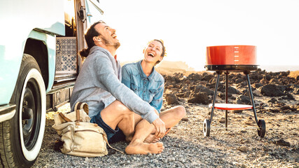 Hipster couple traveling together with oldtimer mini van transport - Travel life style concept with indie people on minivan adventure trip having fun on genuine relax moment - Warm bright filter
