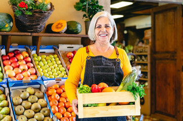 Female greengrocer working at the market holding a box containing fresh fruits and vegetables - Food retail concept
