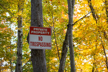 Sign private property no trespassing posted on a tree in a rural area forest surrounded by fall colorful leaves. Selective focus.
