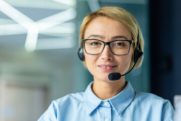 Portrait of successful female online customer support worker, close-up businesswoman smiling and looking at camera, helpline specialist using headset for video call and customer consultation.