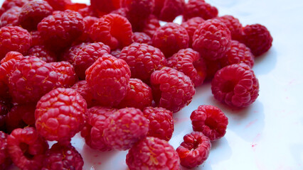 Red berries of ripe juicy large raspberries are scattered on a white table. Vitamin dessert. Berries for a snack