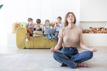 Young mother meditating on the floor while her children playing on background	