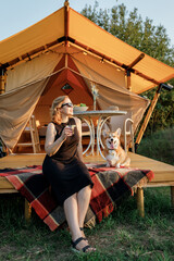 Obraz na płótnie Canvas Happy young woman with Welsh Corgi Pembroke dog relaxing in glamping on summer day. Luxury camping tent for outdoor recreation and recreation. Lifestyle concept