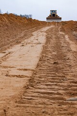 Sand subbase and bulldozer tracks prints. Road construction site. Machine on background in focus, foreground blurred
