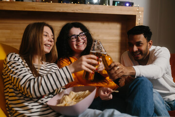A group of friends watch a comedy movie sitting on soft bean bags with drinks and snacks.