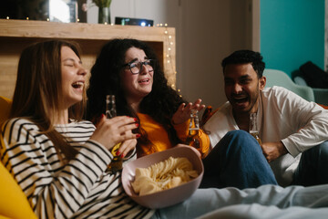 A group of friends watch a comedy movie sitting on soft bean bags with drinks and snacks.