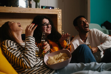 A group of friends watch a comedy movie sitting on soft bean bags with drinks and snacks.