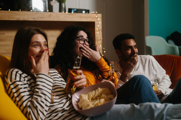 A group of friends watch a comedy movie sitting on soft bean bags with drinks and snacks.