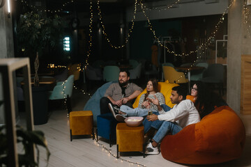 Four friends have fun in the evening in a cafe. They are watching a TV show or a football match.