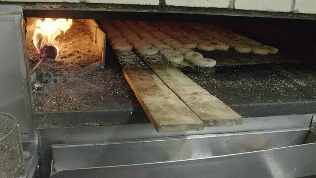 Close-up view of hands placing bagels on wooden decks in a fire oven