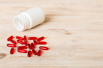 Fototapeta premium Red pills spilled around a pill bottle. Medicines and prescription pills flat lay background. Red medical capsules