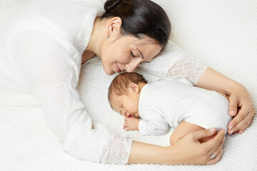 Obraz na płótnie Canvas Smiling Mother sleep with Newborn on White Blanket. Dreaming Mom hugging Baby lying down on Stomach. Happy Motherhood and Parenting. Infant Health Care. Child Protection