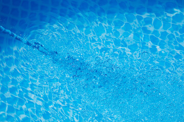Filling a pool with fresh water. Water movement and focus on air bubbles, blue clear water background with copy space