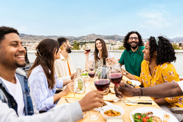 Happy multiracial young adult friends eating and drinking at barbecue party at rooftop in summer....