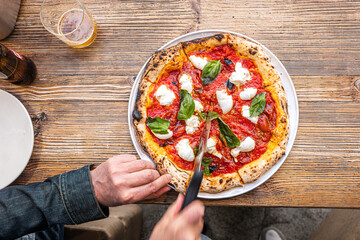 Male hands cutting a freshly baked Neapolitan Margherita Pizza on a rustic wooden table in a...