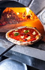 Pizzaiolo pulls out a freshly baked Neapolitan Margherita Pizza from traditional wood-fired oven.