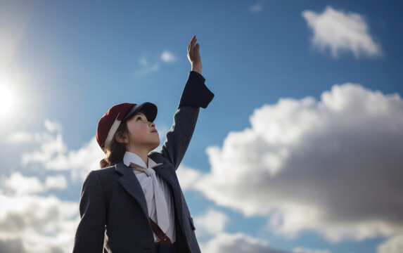 A little girl is playing wearing a hat and jacket raises her hand towards blue sky