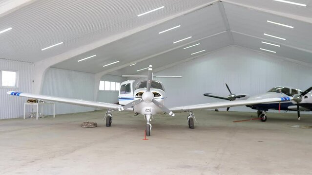 Front view of single engine propeller airplane standing in a closed aircraft hangar. Transportation for tourists and locals. Small white airplane existing hangar preparing for flight. 